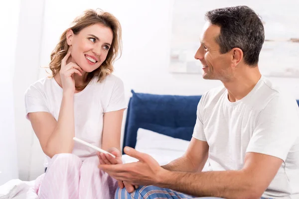 Portrait of happy couple with pregnancy test looking at each other at home — Stock Photo