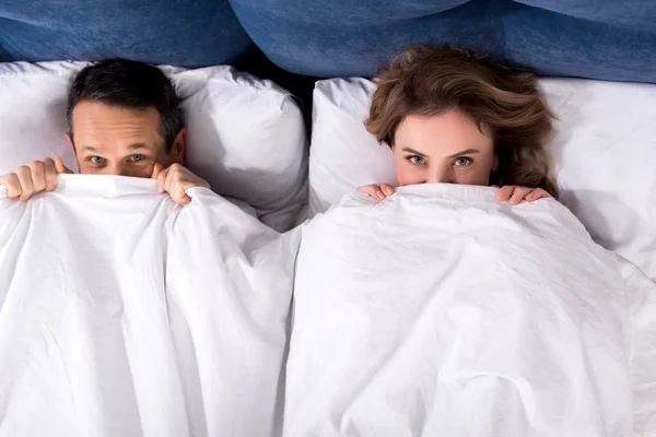 Vue aérienne de la femme et du mari se cachant sous la couverture alors qu'ils étaient couchés au lit à la maison — Photo de stock