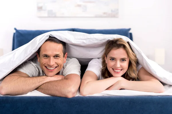 Portrait de femme souriante et mari sous couverture couché sur le lit à la maison — Photo de stock