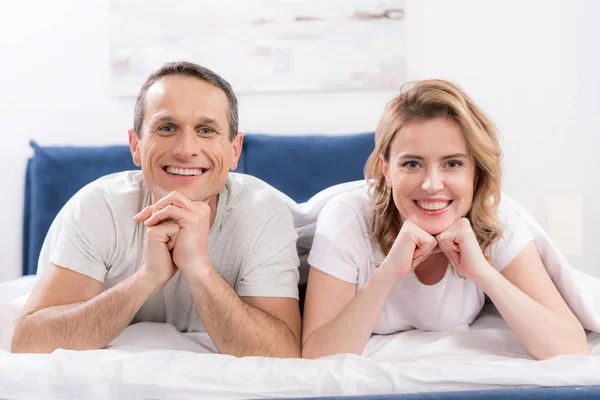 Retrato de esposa sorridente e marido sob cobertor deitado na cama em casa — Fotografia de Stock