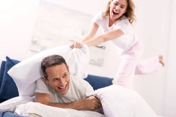 Feliz pareja teniendo almohada lucha en dormitorio en casa - foto de stock