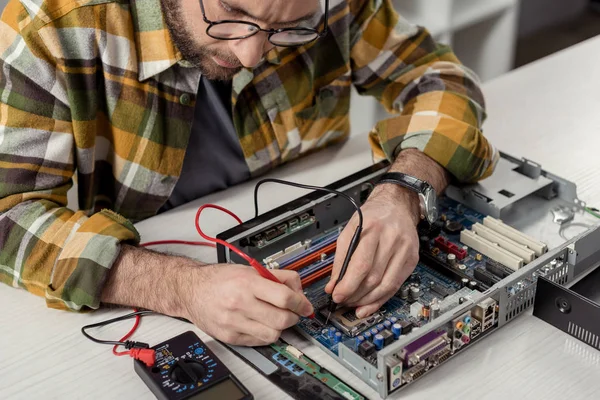 Reparador de imagen recortada utilizando multímetro mientras que la fijación de la placa base de la computadora - foto de stock