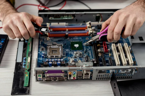 Abgeschnittenes Bild von Händen mit Zangen, die das Motherboard des PCs fixieren — Stockfoto