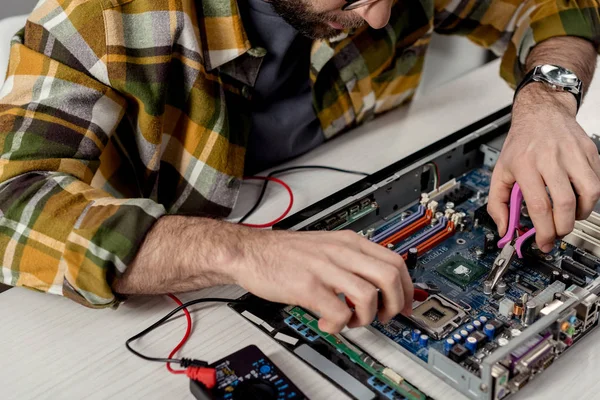 Hombre usando multímetro y pinzas mientras que fija la PC - foto de stock