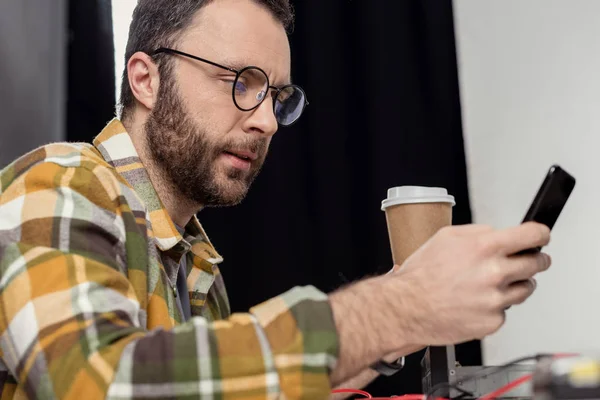 Homem em óculos com café para ir usando smartphone — Fotografia de Stock