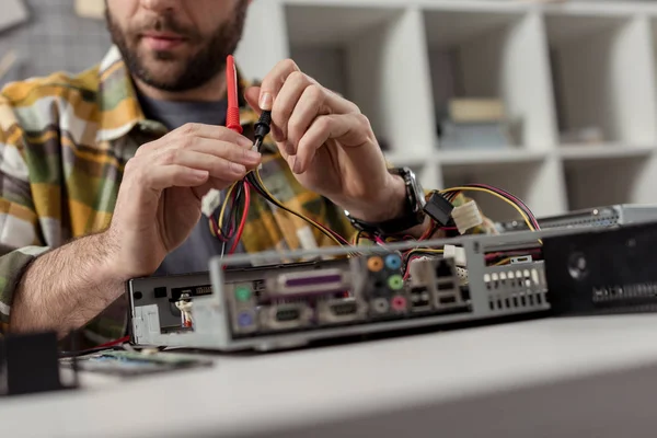 Abgeschnittenes Bild eines Mannes, der Drähte in Händen hält, während er Computer repariert — Stockfoto