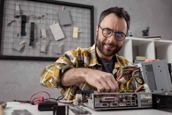 Lächelnder Mann, der Details anpasst, während er Computer repariert — Stockfoto