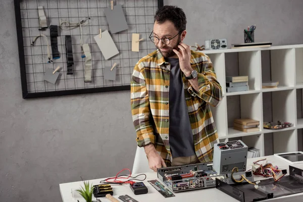 Reparador com a mão na bochecha olhando para longe sobre computador quebrado na mesa — Fotografia de Stock