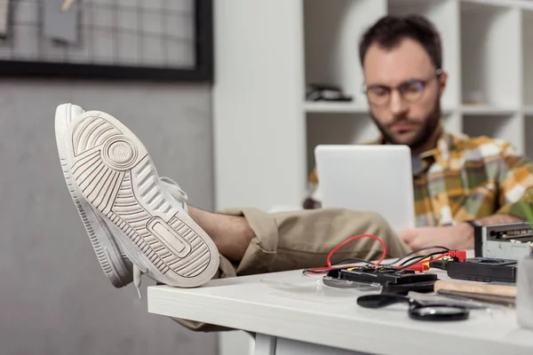 Mann benutzt digitales Tablet, während er auf Stuhl mit Beinen auf Tisch sitzt — Stockfoto