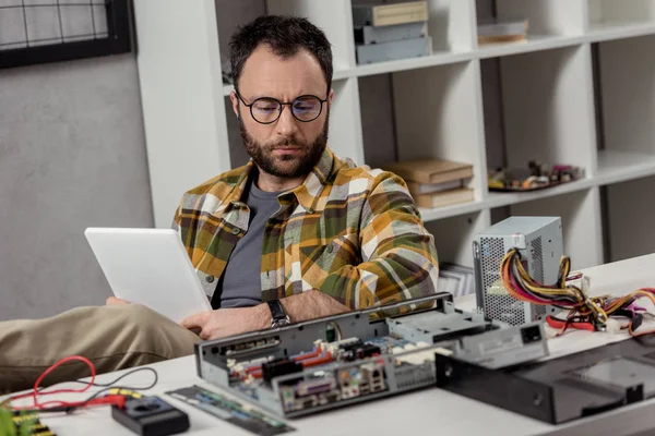 Mann sitzt mit digitalem Tablet gegen kaputten PC auf Tisch — Stockfoto