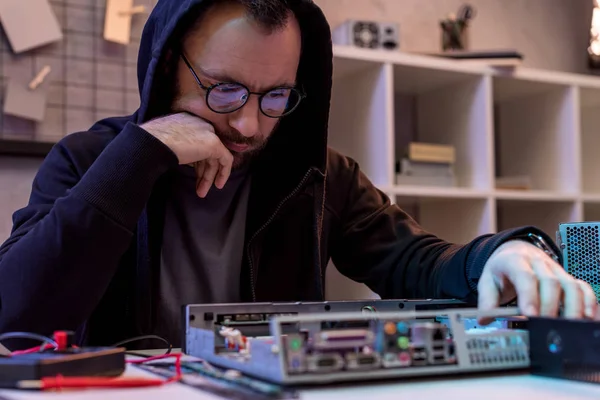 Mann im Kapuzenpulli mit Hand am Kinn blickt auf Computer — Stockfoto