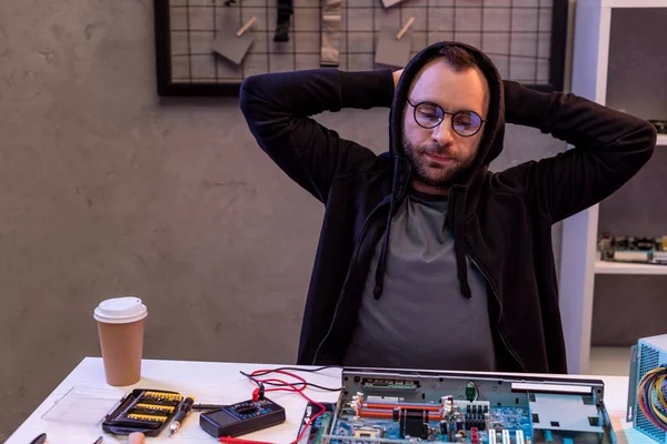 Uomo con le mani dietro la testa guardando sulla scheda madre del computer — Foto stock