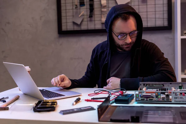 Mann im Kapuzenpullover benutzt Laptop, während er auf kaputten PC schaut — Stockfoto