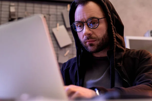 Людина в окулярах використовує ноутбук, сидячи — стокове фото