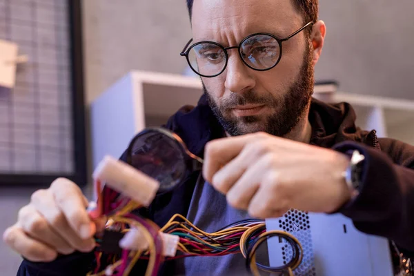 Hombre usando lupa mientras sostiene cables en la mano - foto de stock