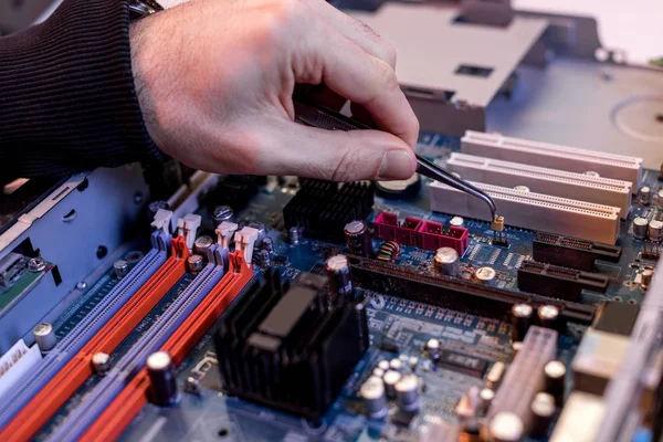 Abgeschnittenes Bild der Hand mit einer Zange, die Details auf dem Motherboard anpasst — Stockfoto