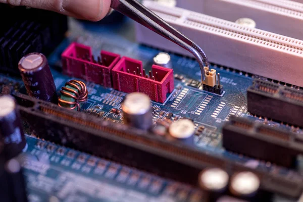 Cropped image of hand with tweezers adjusting detail on motherboard — Stock Photo