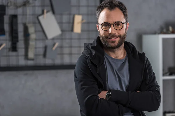 Lächelnder Mann mit Brille blickt mit verschränkten Armen in die Kamera — Stockfoto