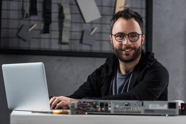 Smiling man looking at camera while using laptop — Stock Photo