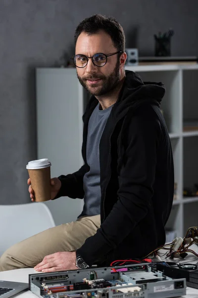 Mann mit Kaffee in der Hand sitzt auf Tisch mit kaputtem PC — Stockfoto