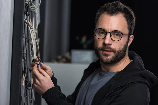 Hombre en gafas mirando a la cámara mientras sostiene los cables contra la pared - foto de stock