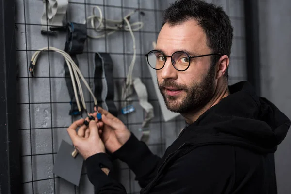 Man in glasses looking at camera while holding wires against wall — Stock Photo