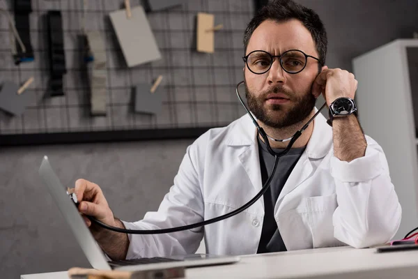 Man in white coat and stethoscope diagnosing laptop — Stock Photo