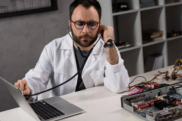 Homem de casaco branco e estetoscópio diagnosticando laptop — Fotografia de Stock