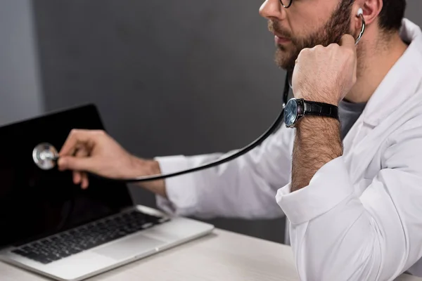 Cropped image of repairman in doctor white coat and stethoscope diagnosing laptop — Stock Photo