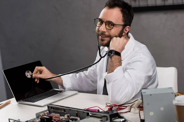 Homem sorridente em vestido de casaco branco e estetoscópio diagnosticar laptop — Fotografia de Stock