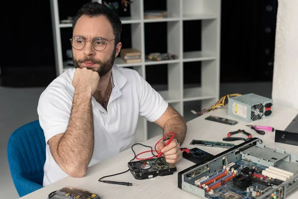 Pensive repairman with nand on chin using multimeter  while fixing hard disk drive — Stock Photo