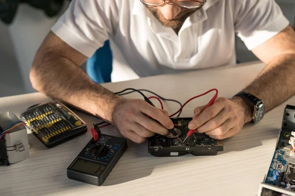 Hombre con multímetro comprobando parte de la computadora en la mesa - foto de stock