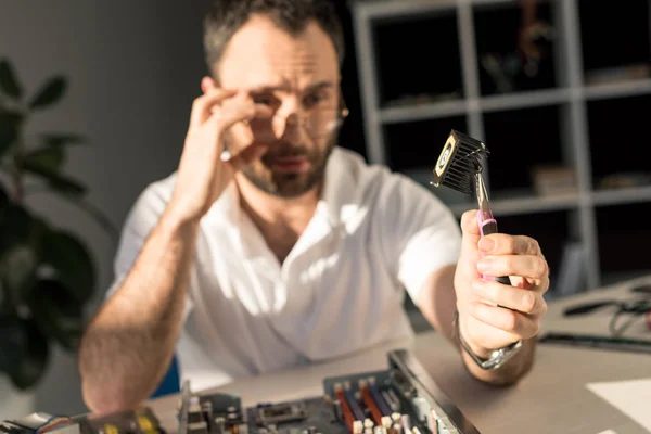 Homem segurando parte do computador na mão com pinças — Fotografia de Stock