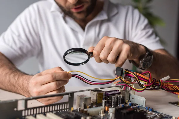 Imagen recortada del hombre usando lupa mientras sostiene los cables en la mano - foto de stock