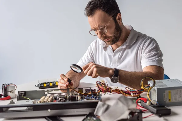 Man using magnifier while holding wires in hand — Stock Photo