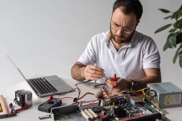 Homme utilisant multimètre tout en fixant ordinateur cassé et regardant vers le bas — Photo de stock