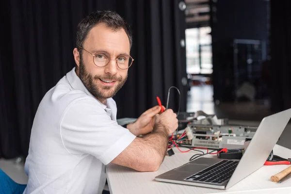 Lächelnder Mann, der in die Kamera schaut, während er das Multimeter in den Händen hält — Stockfoto