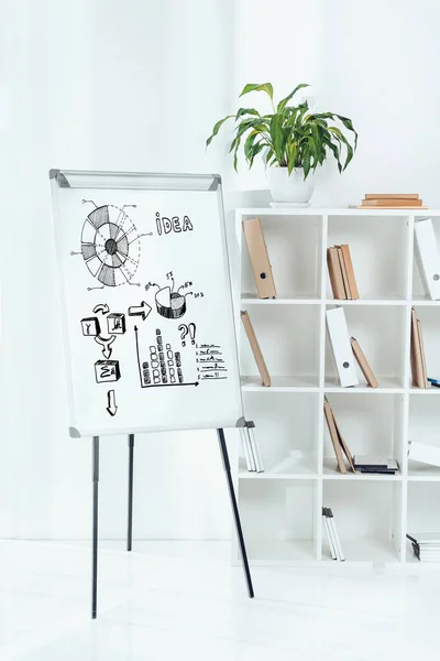 Whiteboard with business idea icons and wooden shelves with folders in office — Stock Photo