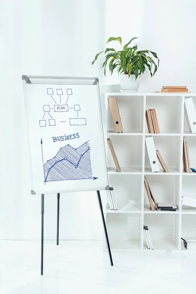 Tableau blanc avec graphique de plan d'affaires et étagères en bois avec des dossiers dans le bureau — Photo de stock