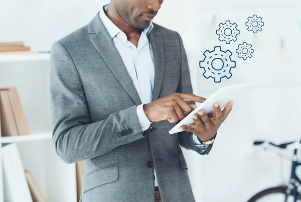 Cropped image of african american man using digital tablet and cogwheels icons — Stock Photo