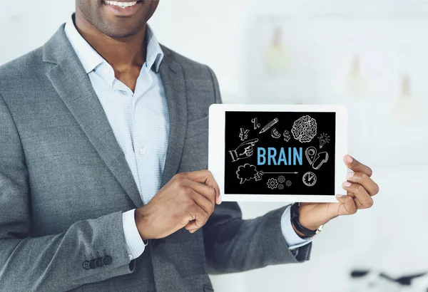 Image recadrée de souriant homme afro-américain montrant tablette numérique avec mot cerveau et icônes créatives — Photo de stock