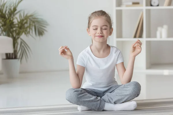 Niño sonriente meditando en pose de loto en casa - foto de stock