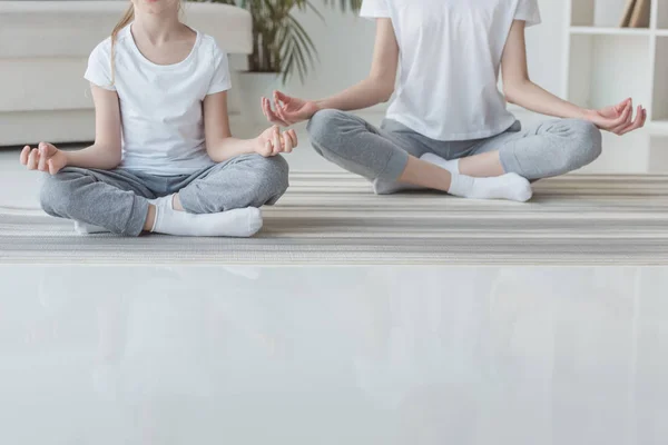 Cropped shot of mother and daughter meditating in lotus pose together at home — Stock Photo