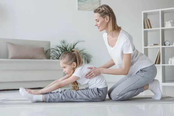 Mother helping her daughter to do forward bend at home — Stock Photo