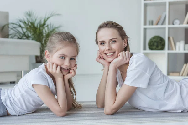Happy mother and daughter lying on floor together and looking at camera — Stock Photo