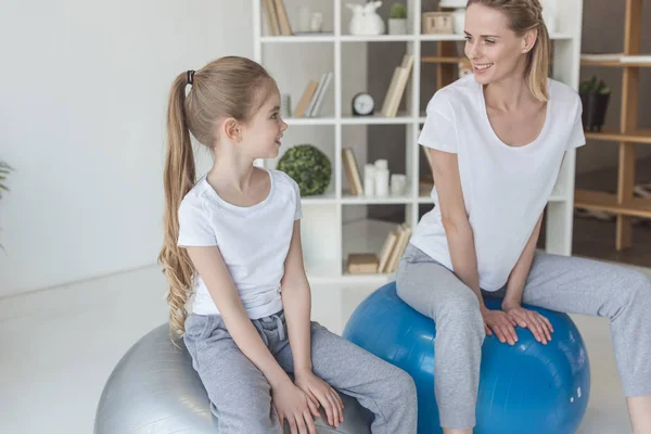 Happy mother and daughter sitting on fit balls at home and looking at each other — Stock Photo