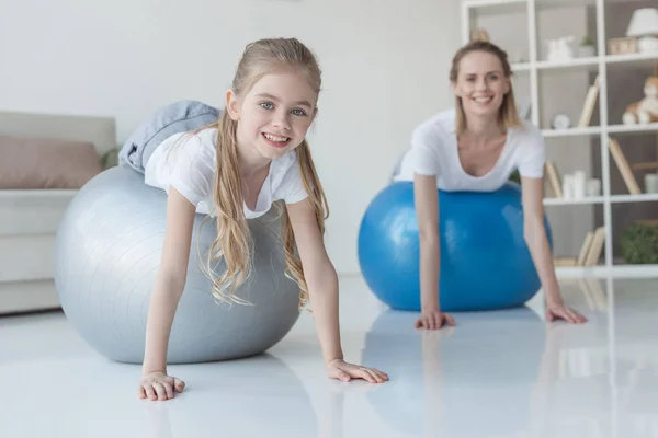 Smiling mother and daughter lying on fit balls at home — Stock Photo