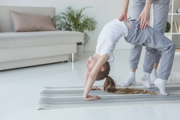Madre enseñando a su hija a ponerse de pie en la rueda de yoga posar en casa - foto de stock