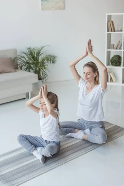 Madre e hija meditando en la pose de loto en casa - foto de stock