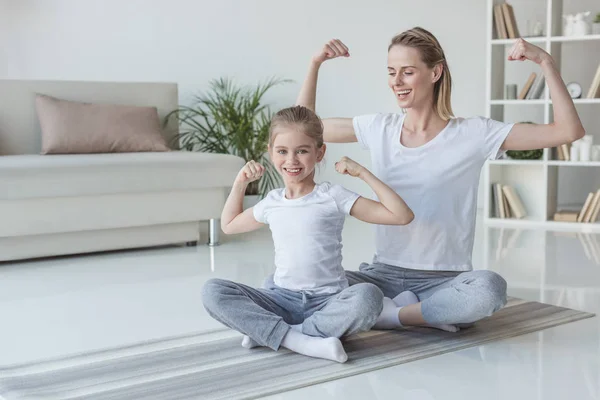 Mother and daughter showing muscles on yoga mats — Stock Photo